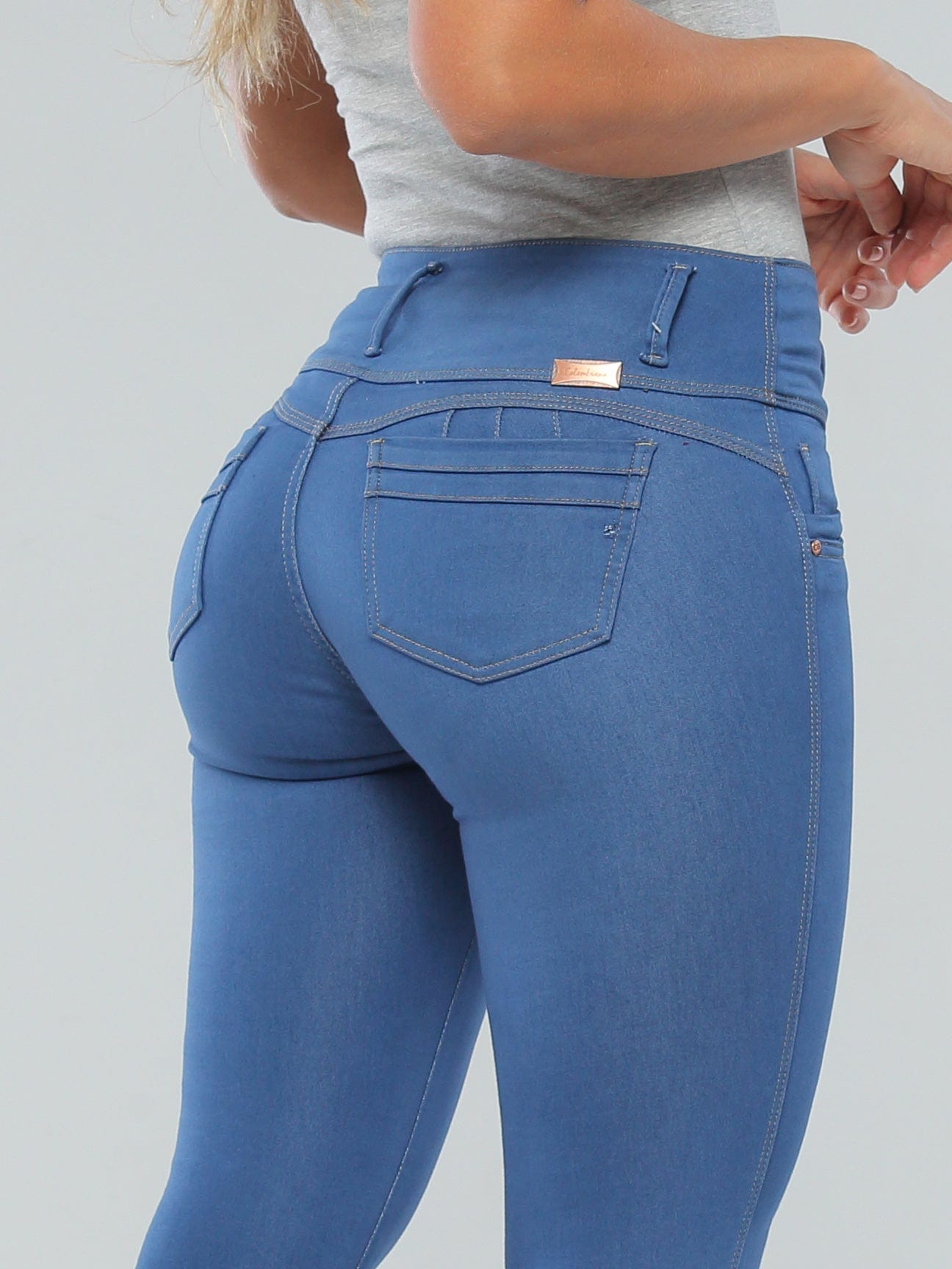 Close up of Latina woman wearing high-waisted blue butt lift jeans with 3D pockets and thick waistband.